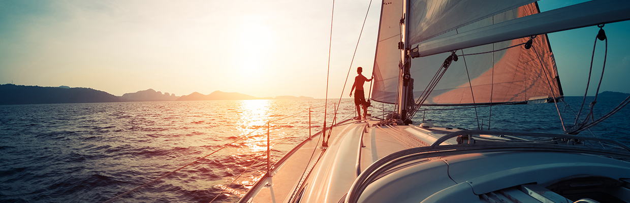 Men at the front of a sailboat at sunset